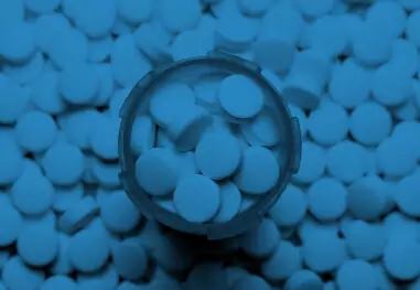 Magnifying glass hovering over blue pill capsules on blue background