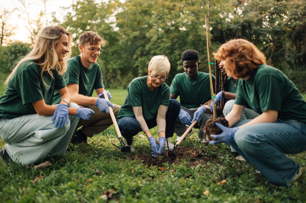 Group of volunteers in green shirts planting tree together outdoors
