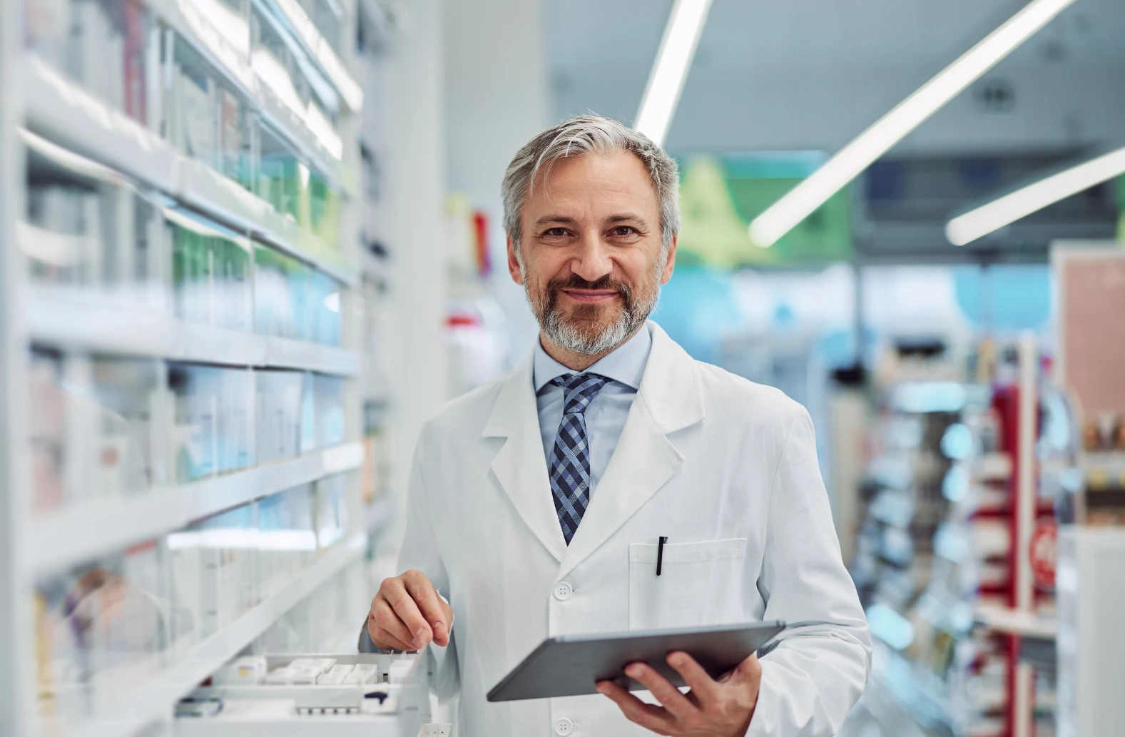 Pharmacist holding tablet in white coat at pharmacy shelves
